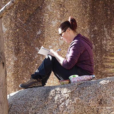 Teacher sitting on a rock taking notes